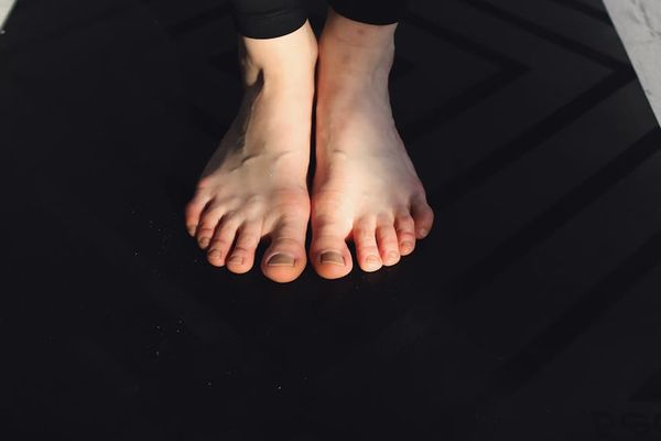 Close up of hands stretching towards feet on purple mat.